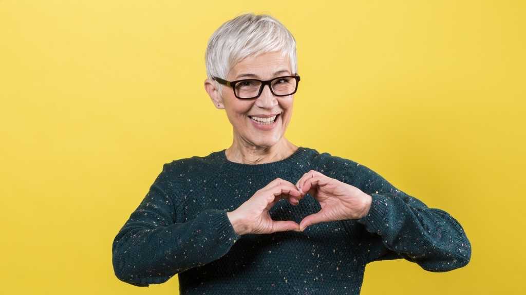 An older woman smiling and making a heart shape with her hands